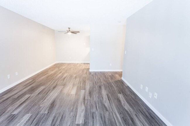 Empty living room with wood-look flooring, light gray walls, and an open kitchen area.
