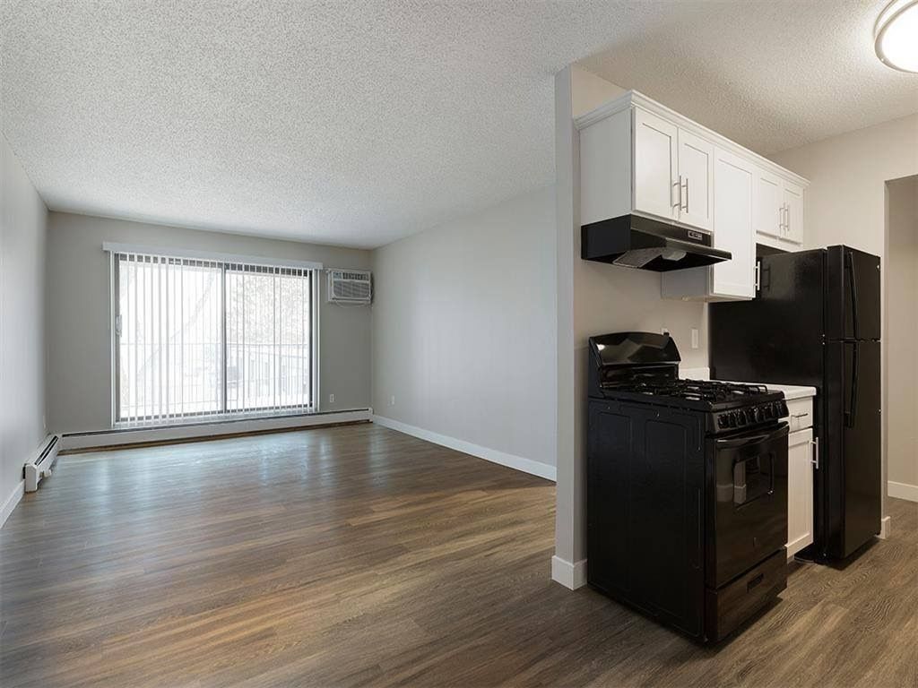 Open living area with kitchen; white cabinets, black appliances, and a large window with blinds.