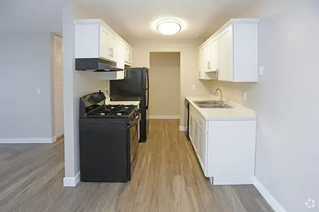 Kitchen with white cabinets, black appliances, and light wood-look flooring.