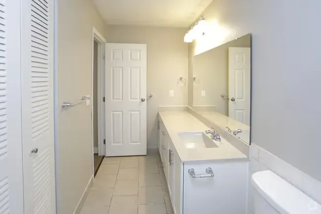 Bathroom with white vanity, large mirror, white tile floor, and a closed door.