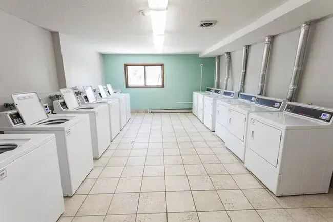 Laundry room with rows of white washers and dryers, tiled floor, and small window.