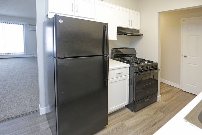 Black refrigerator, stove, and white cabinets in a kitchen with light wood flooring.