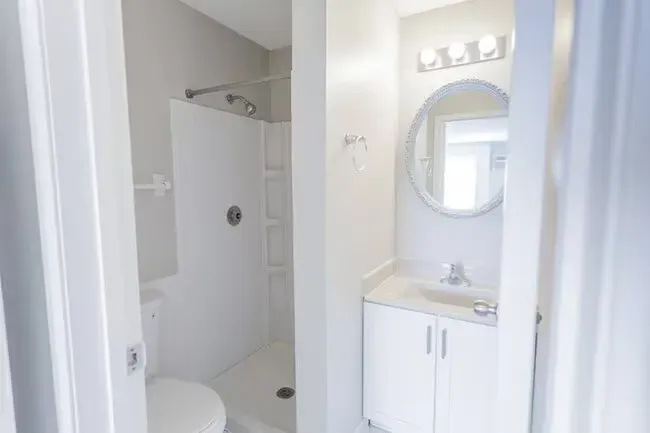 Bathroom with white shower stall, vanity, and toilet, seen through an open doorway.