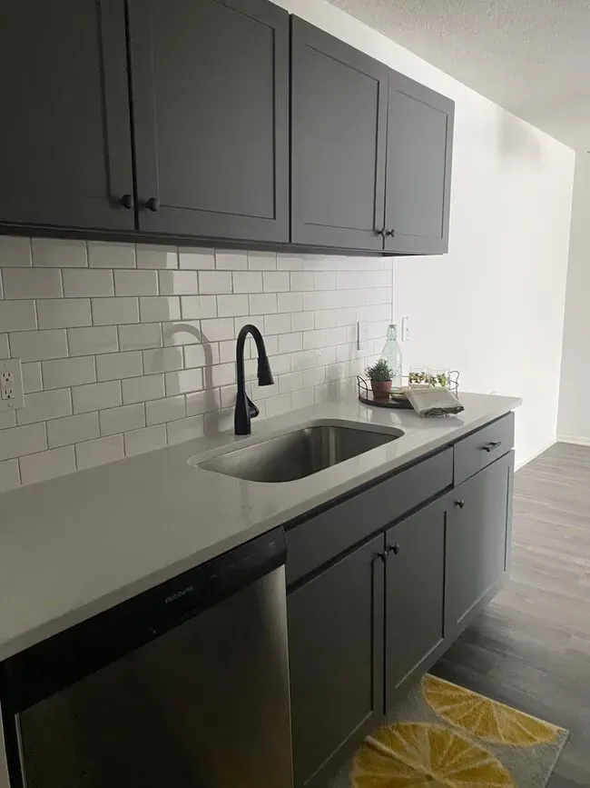 Kitchen with dark gray cabinets, white subway tile, and a stainless steel sink.
