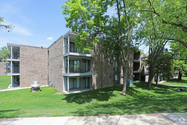 Apartment building with stone facade and balconies, surrounded by green grass and trees.
