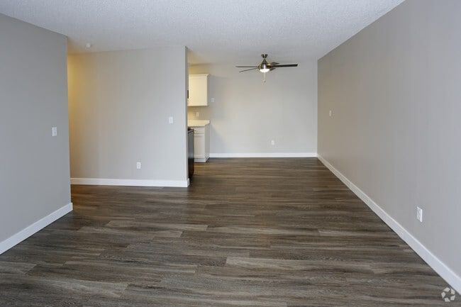 Empty living room with gray walls, wood-look flooring, and a view into the kitchen.