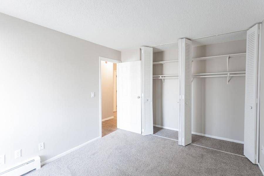 Empty bedroom with open bi-fold closet doors and neutral walls.