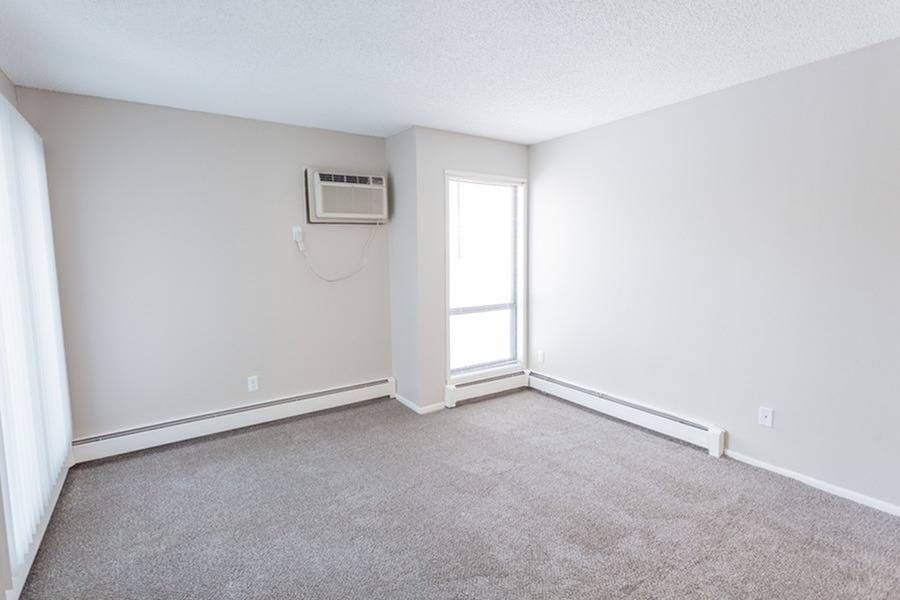 Empty apartment living room with neutral walls, carpet, a window, and a wall-mounted air conditioner.