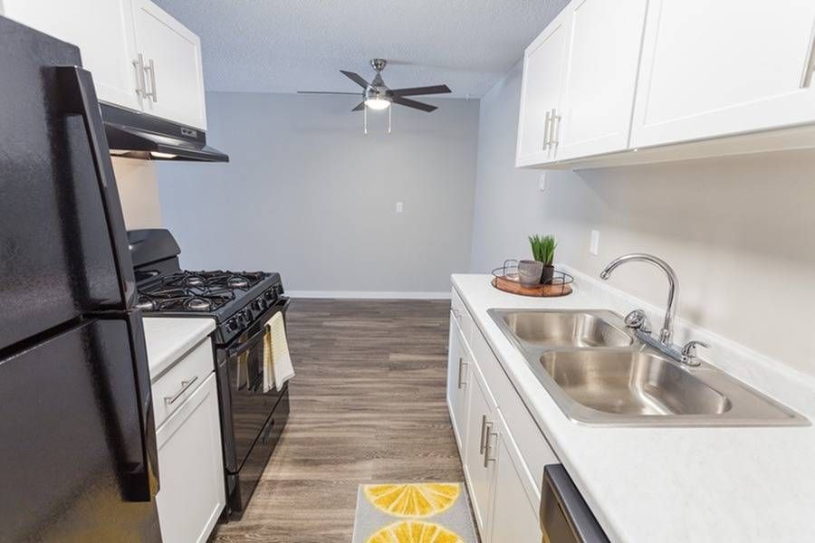 Modern apartment kitchen with white cabinets, stainless steel double sink, and black appliances.
