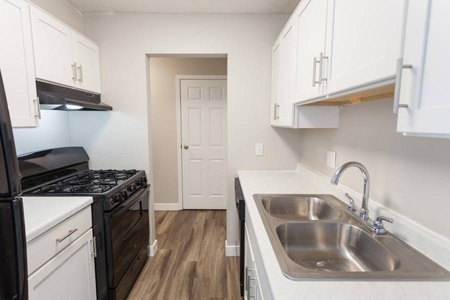 Galley kitchen with white cabinets, double stainless sink, and gas stove in an apartment.