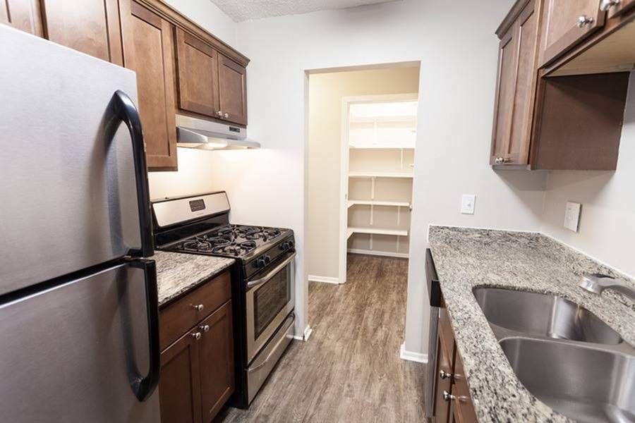 Apartment kitchen with stainless steel fridge, gas range, granite counters, and a double sink.
