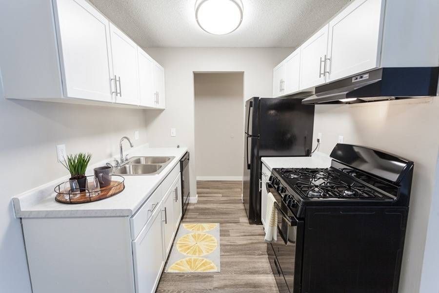 Narrow galley kitchen with white cabinets, stainless sink, and black fridge and stove.
