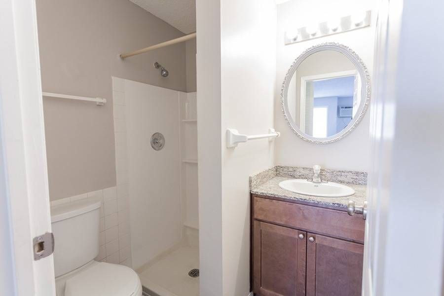 Apartment bathroom with shower stall, toilet, and granite vanity with round mirror.