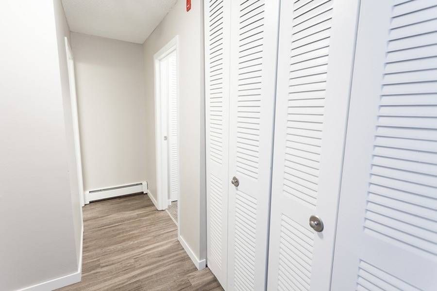 Interior apartment hallway with white walls and white louvered closet doors along a wood-toned floor.