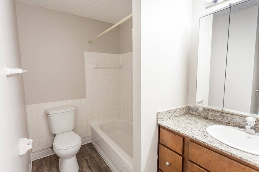 Bathroom featuring a toilet, bathtub with tiled surround, and a granite vanity.