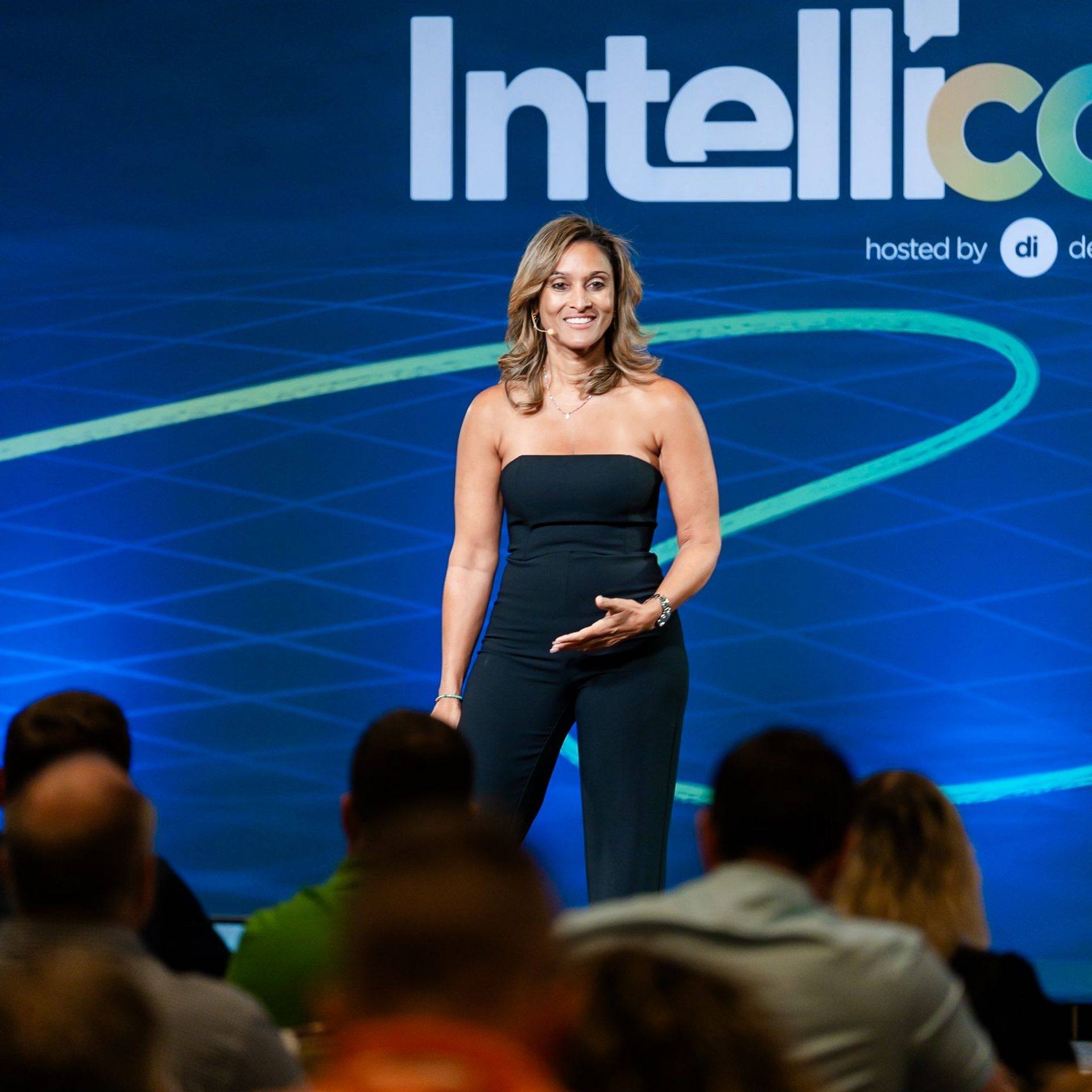 Woman in black jumpsuit on stage speaking at 