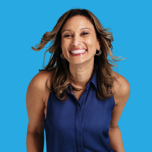 Woman with brown hair smiles broadly, wearing a blue sleeveless top, against a blue backdrop.
