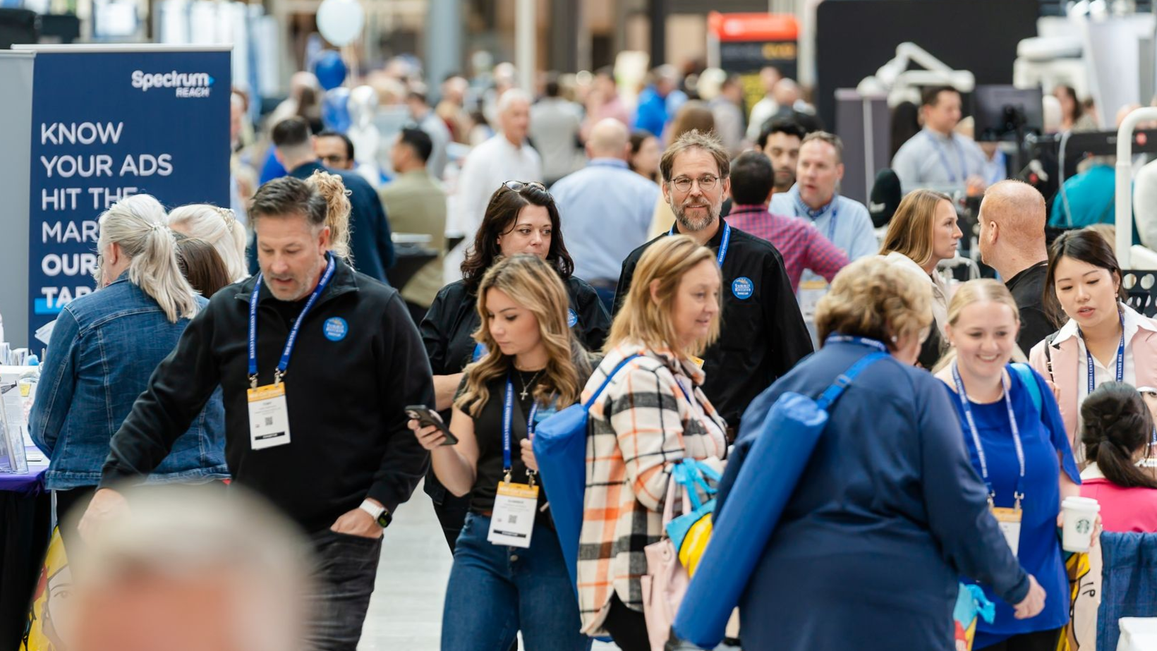 Group of people at an event, smiling and posing.  Some have lanyards. Indoors, bright lighting.