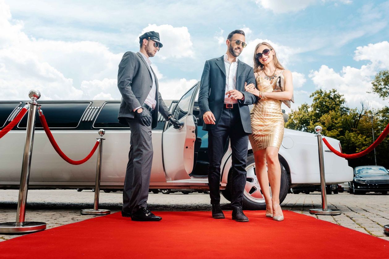 two men and a woman are standing on a red carpet in front of a limousine