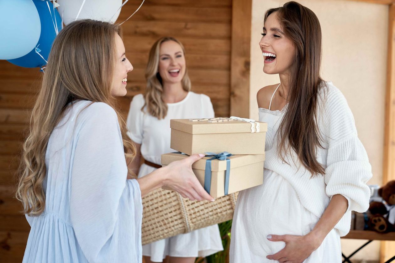 a pregnant woman is receiving gifts from two other women at a baby shower