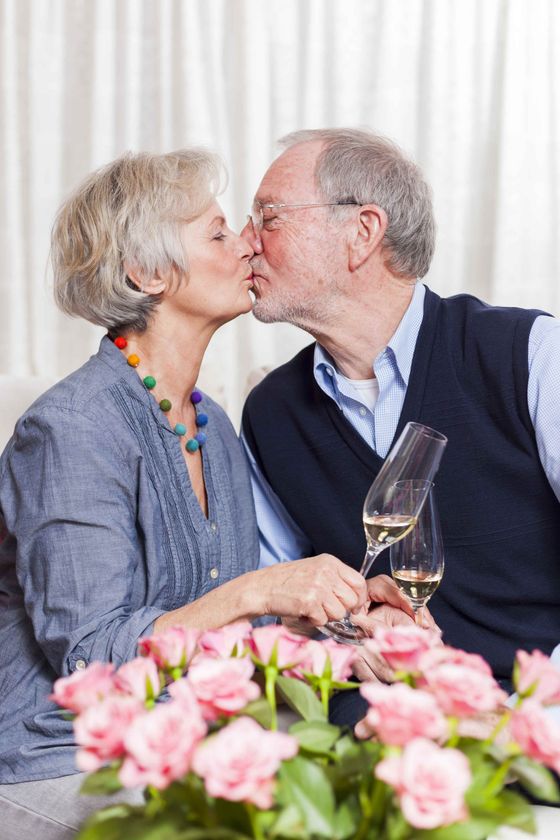 an elderly couple kissing while holding glasses of wine