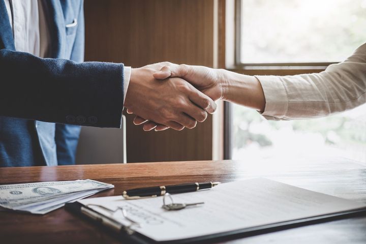 Two people shaking hands over a table with money, keys, and a document.