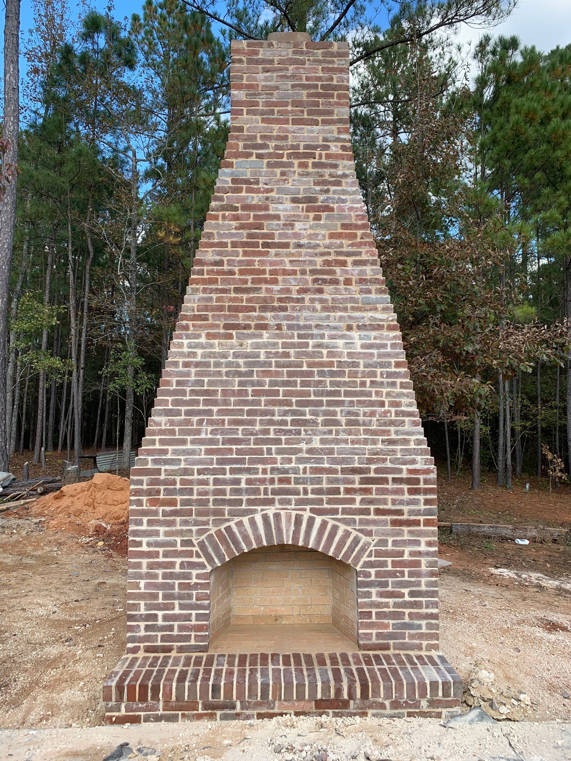 A large brick fireplace is sitting in the middle of a forest.