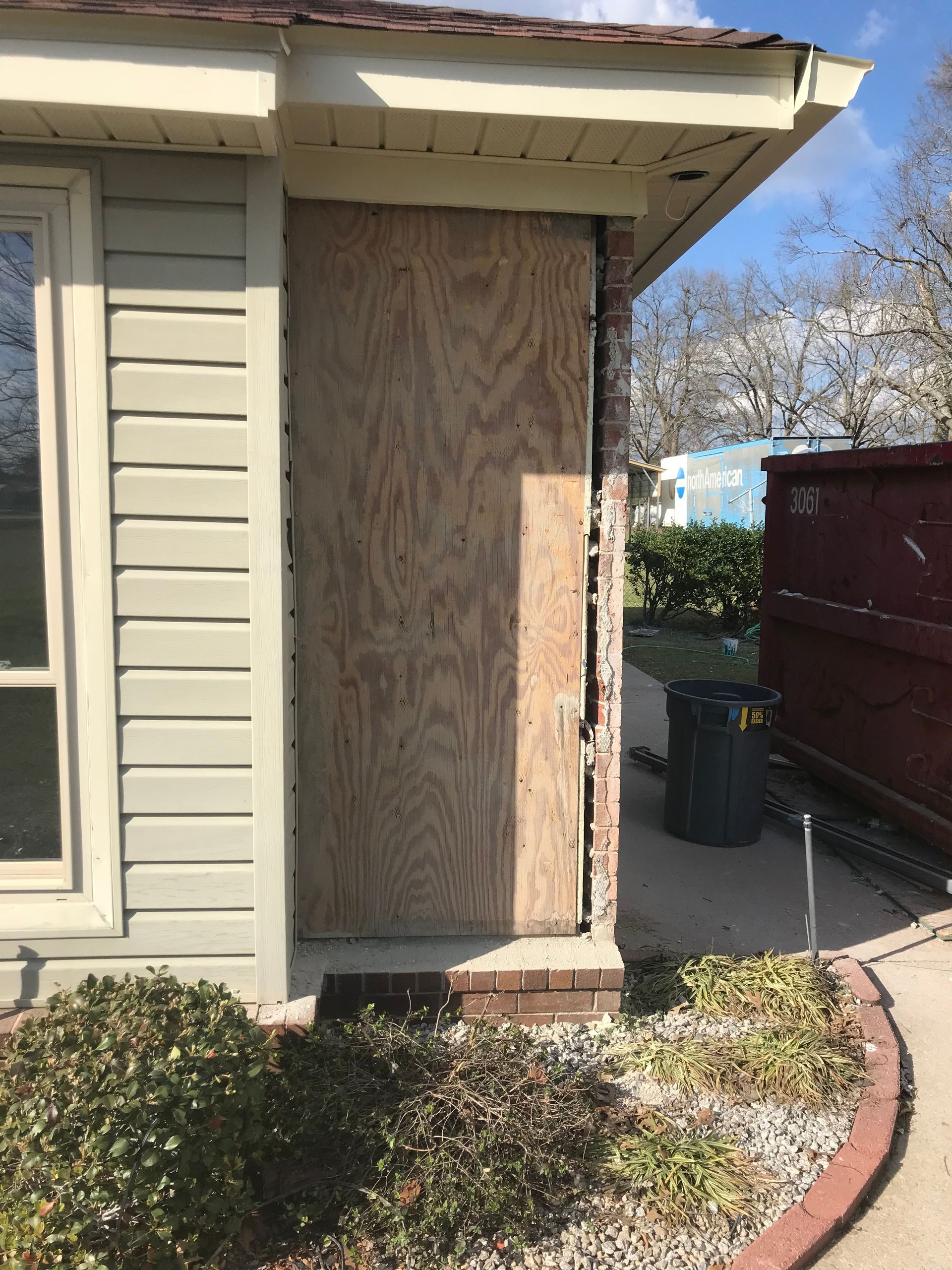 A house with a door boarded up and a dumpster in the background.