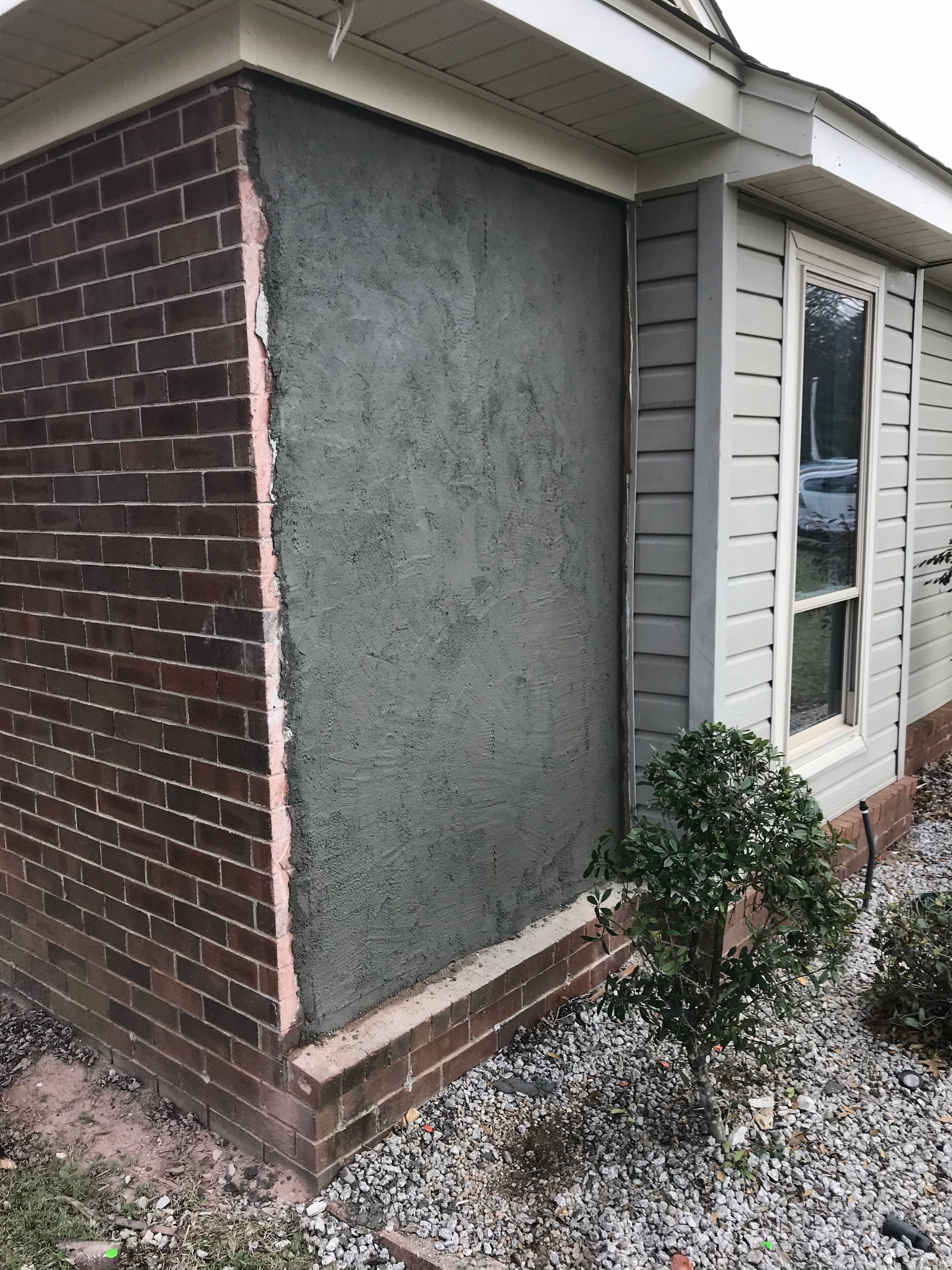 The side of a house with a brick wall and a window.