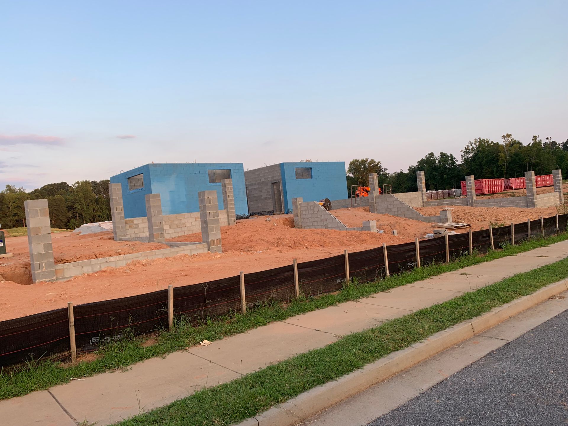 A house is being built on a dirt lot next to a sidewalk.