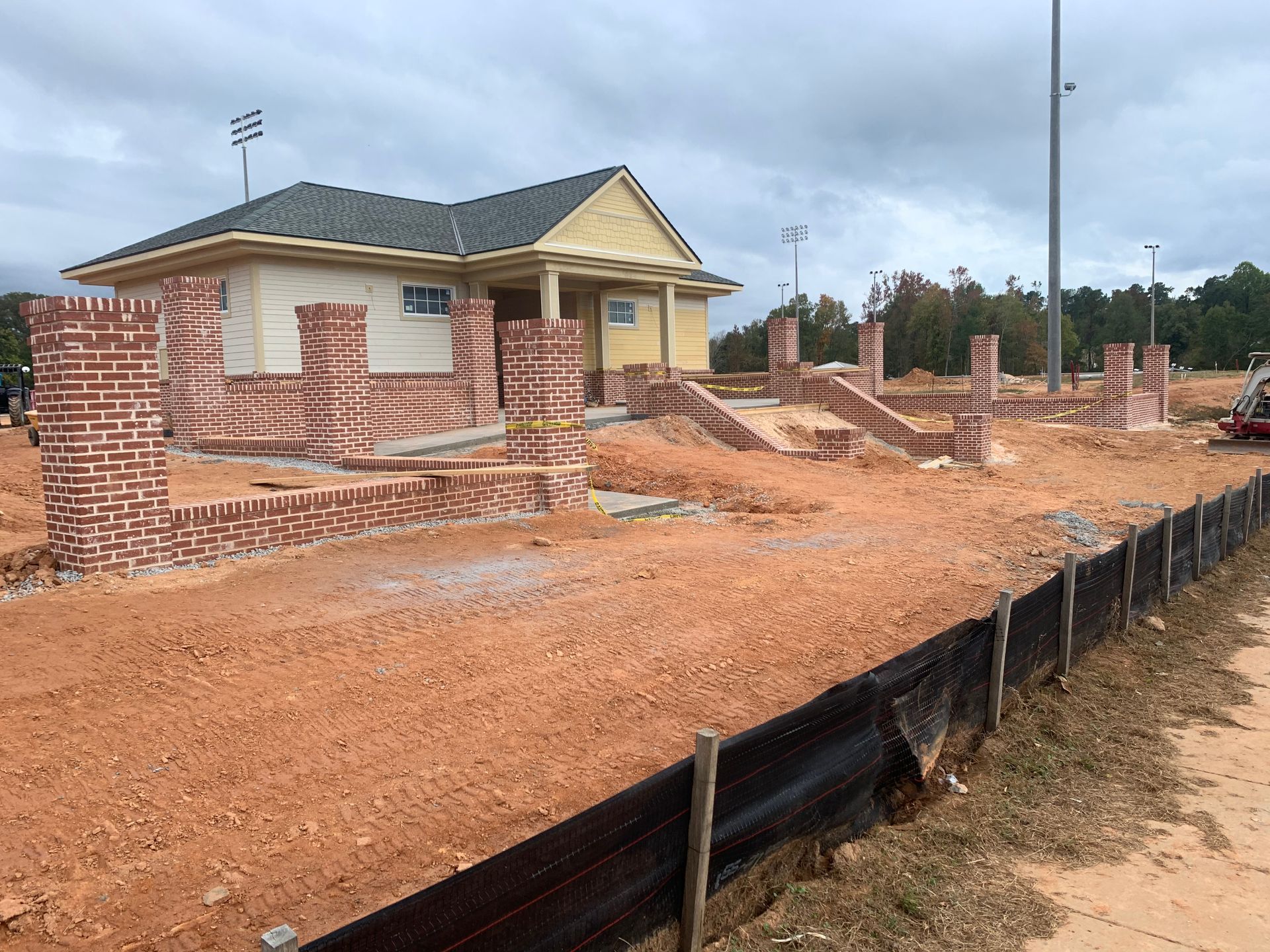 A house is being built in a dirt field next to a black fence.