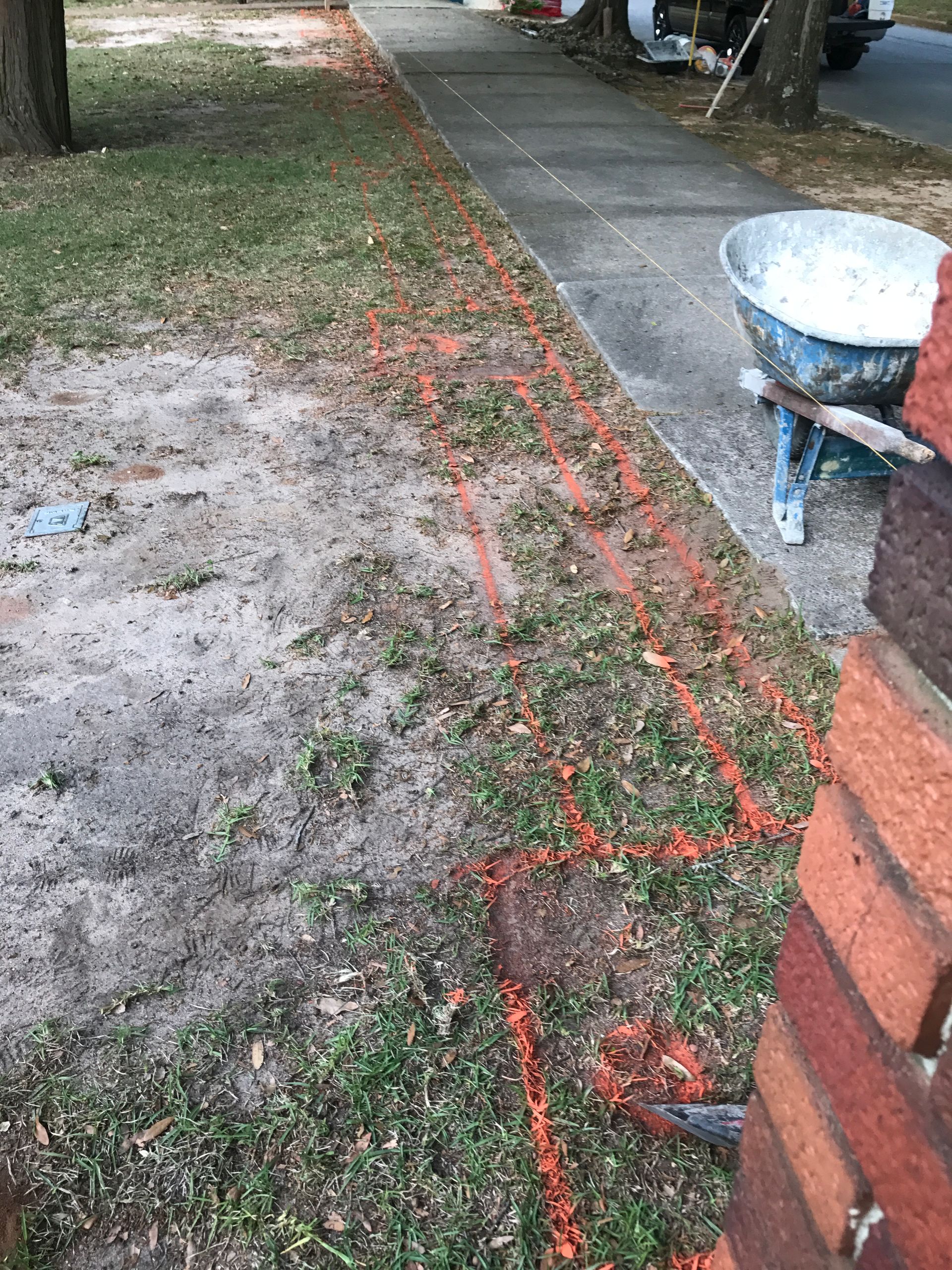 A wheelbarrow is sitting on the side of a sidewalk next to a brick wall.