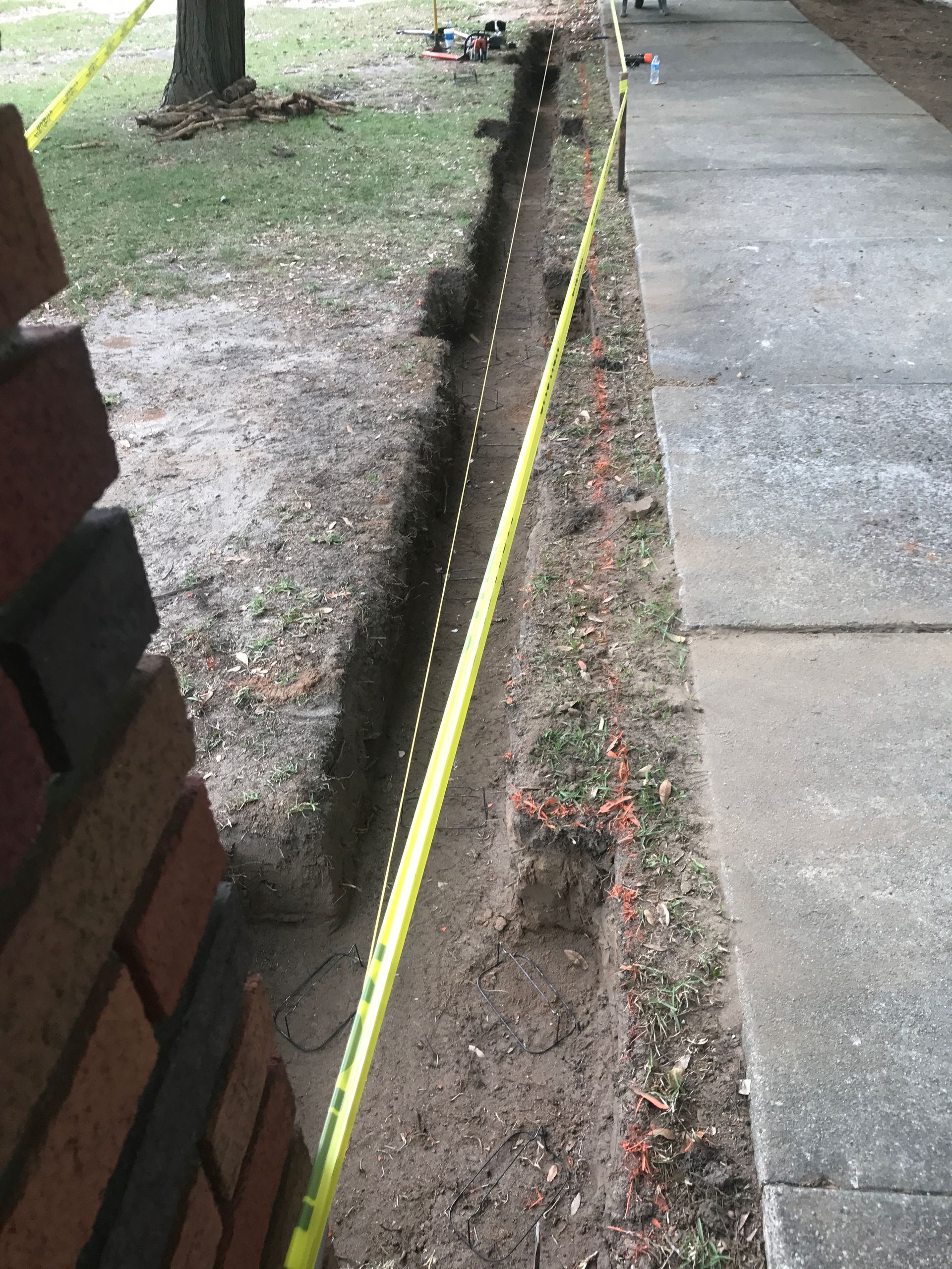 A yellow tape measure is laying on the sidewalk next to a brick wall.