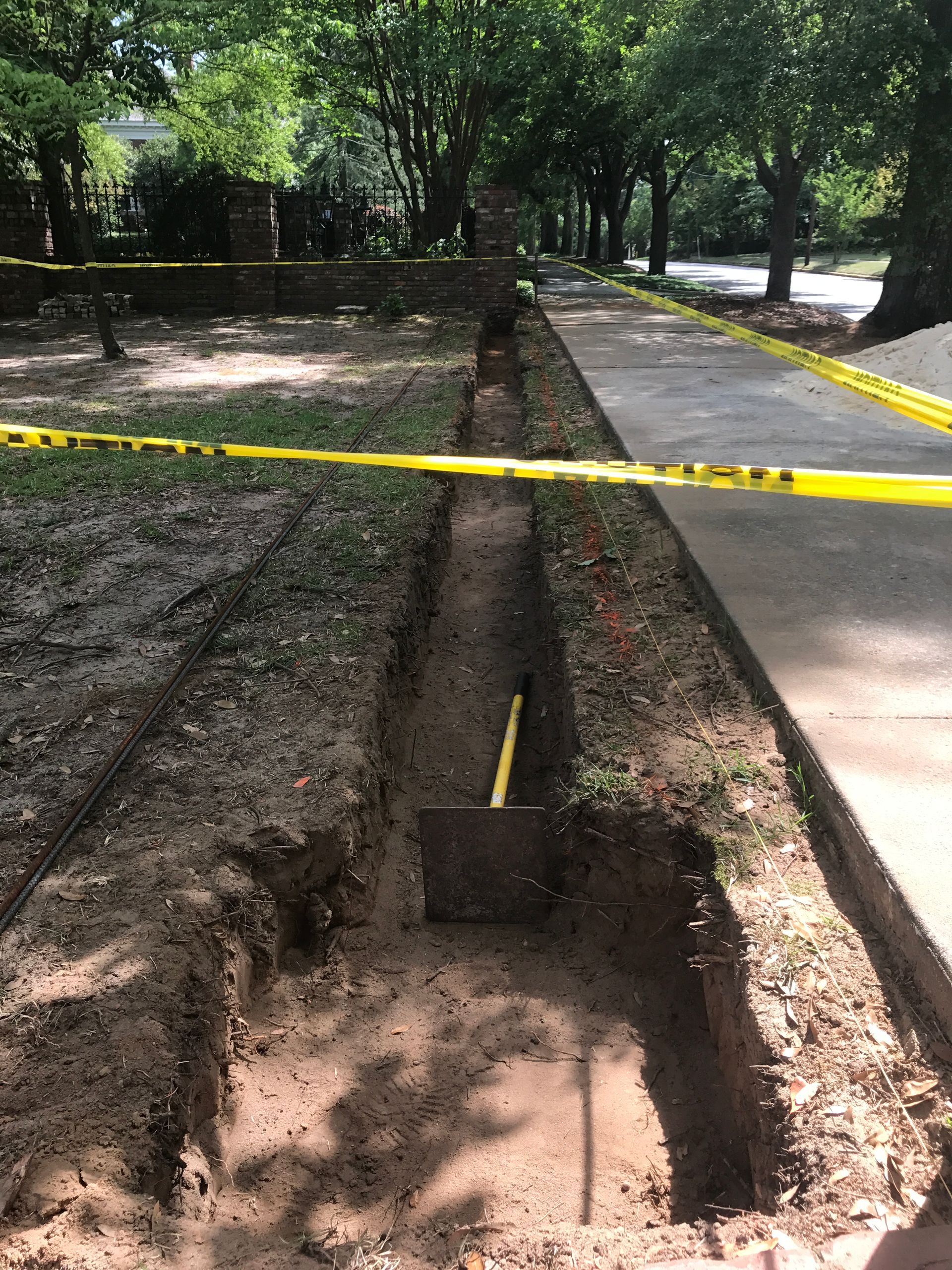 A shovel is digging a hole in the ground next to a sidewalk.