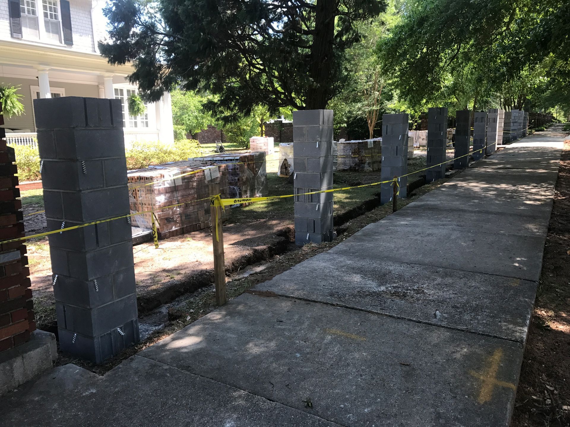 A sidewalk with a fence made of bricks and a house in the background.