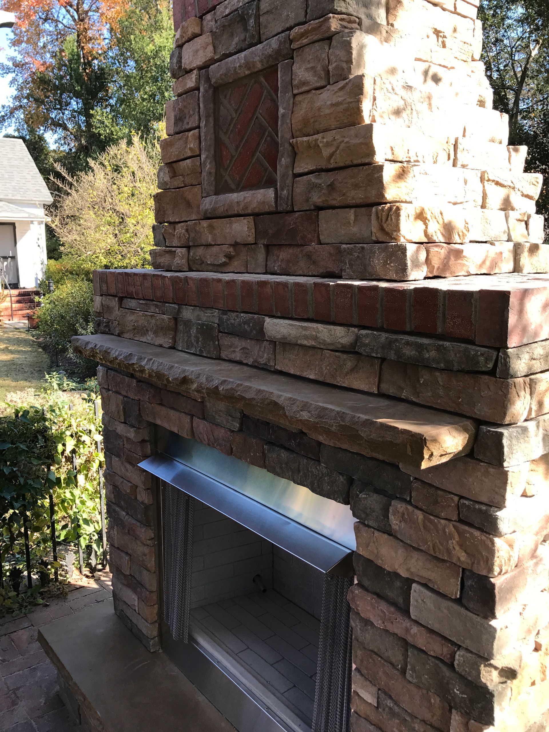 A brick fireplace with a stainless steel mantle is sitting in front of a house.