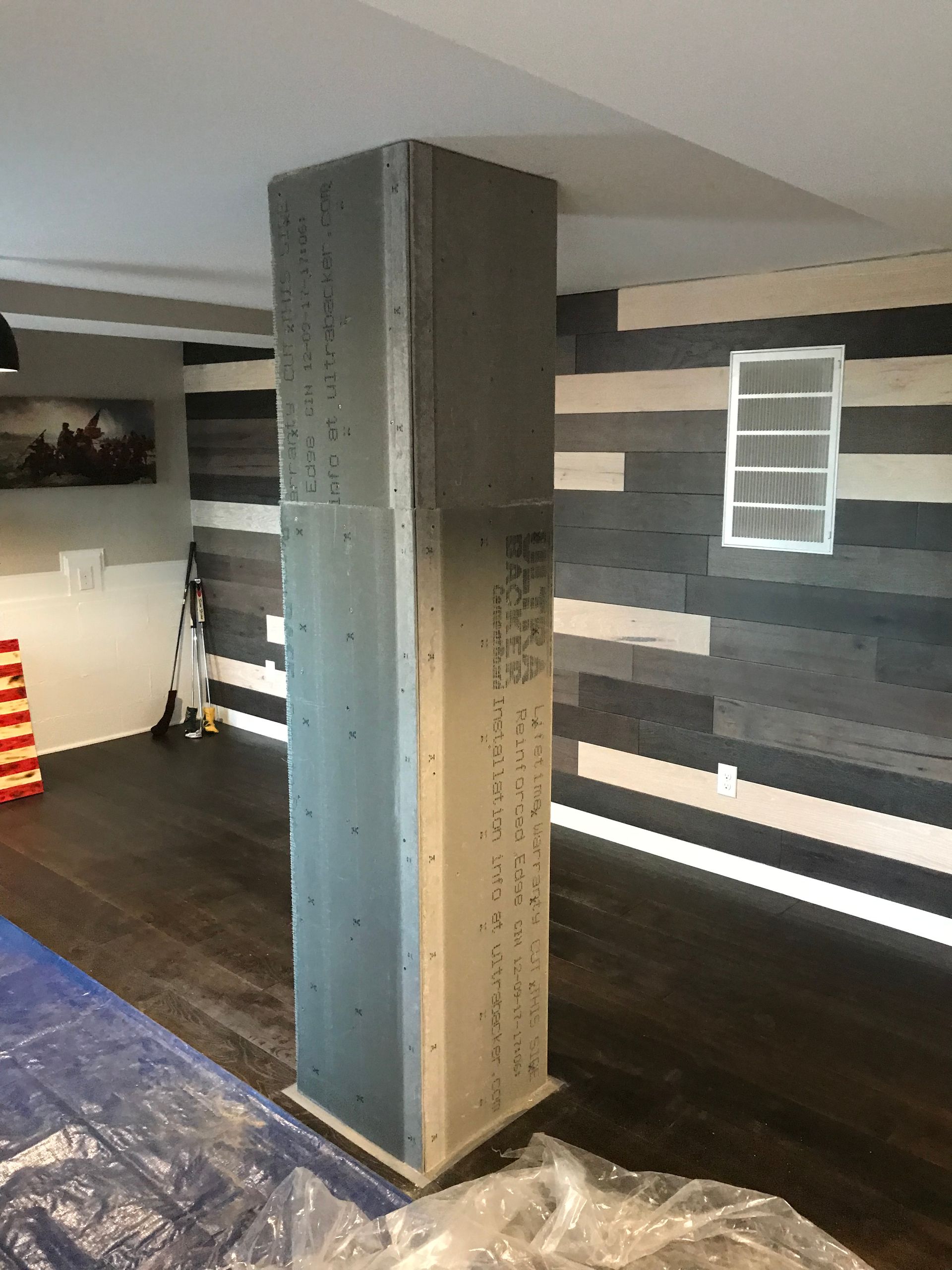 A pillar in a room with a wooden wall behind it.