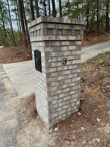 A brick post with a mailbox on it is next to a road.