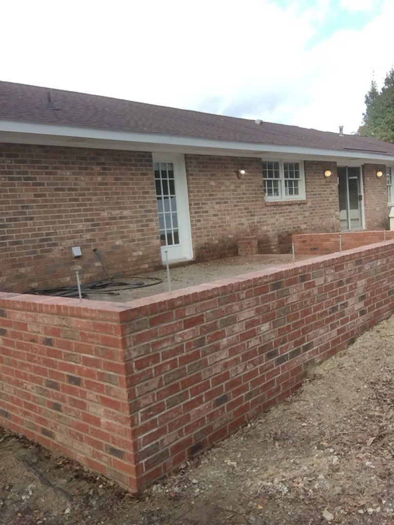 A brick wall is being built in front of a brick house.
