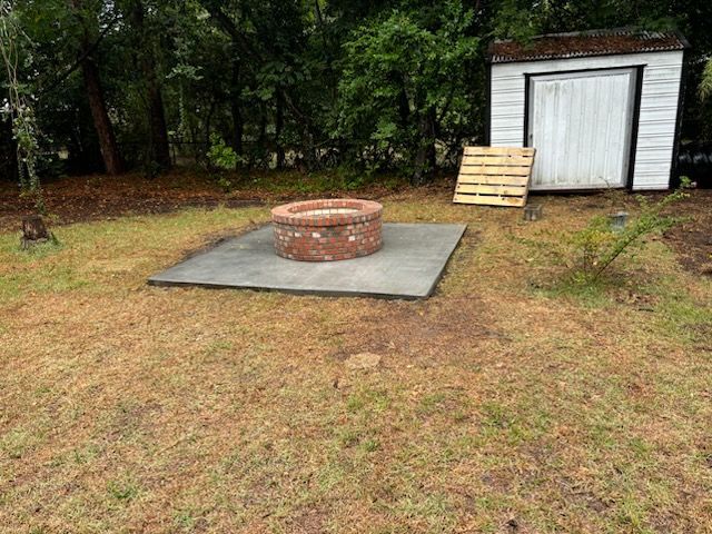 A fire pit is sitting on top of a concrete slab in a yard next to a shed.