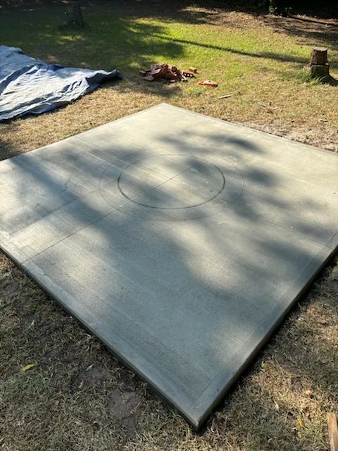 A large square concrete slab with a hole in the middle is sitting on top of a lush green field.