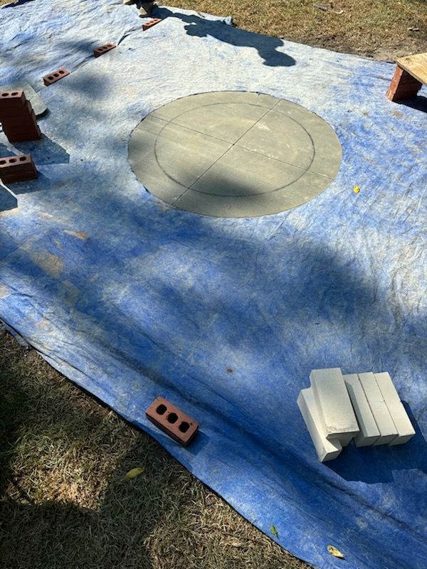 A blue tarp is laying on the ground with bricks on it.
