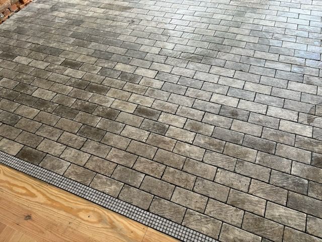 A close up of a brick floor with a wooden floor in the background.