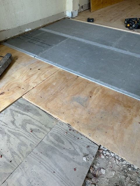A gray tile floor is being installed on a wooden floor