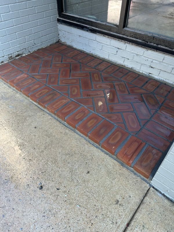 A brick floor with a herringbone pattern is on a sidewalk next to a window.