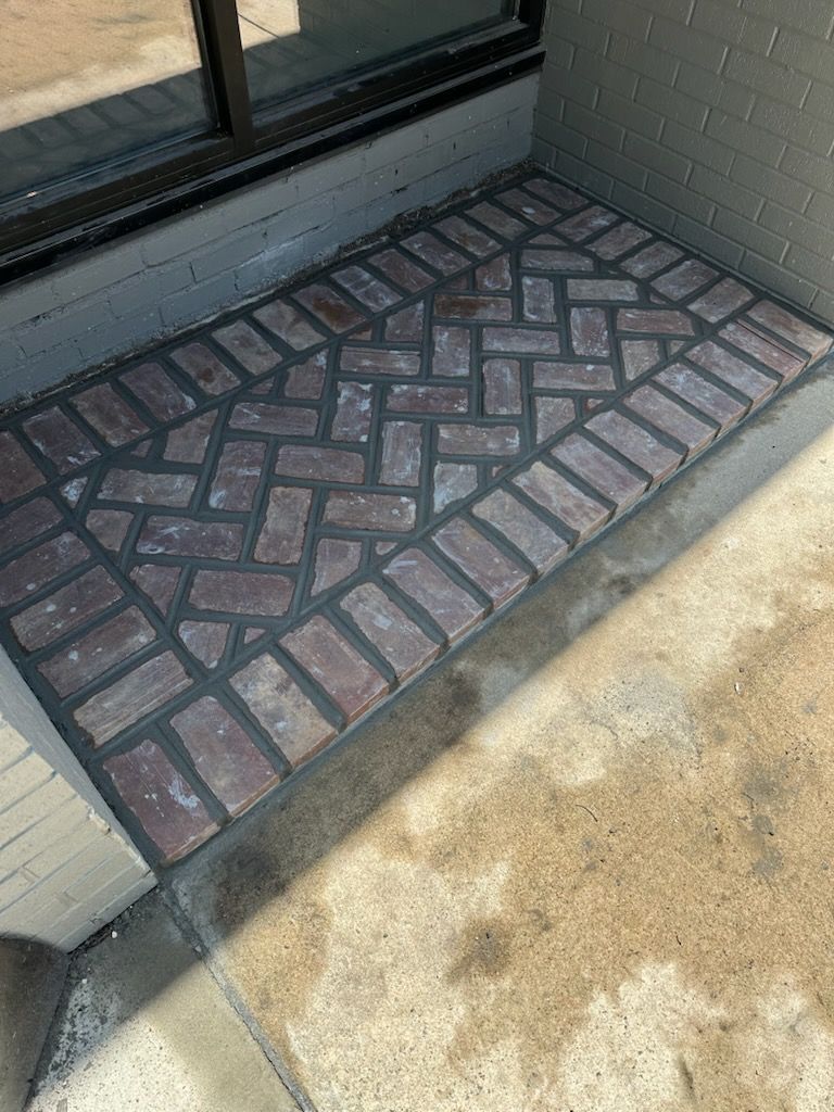 A brick walkway on the side of a building next to a window.