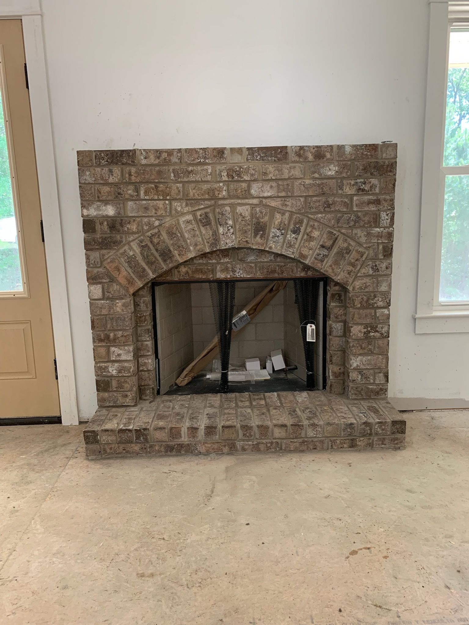 A brick fireplace is sitting in a living room next to a window.