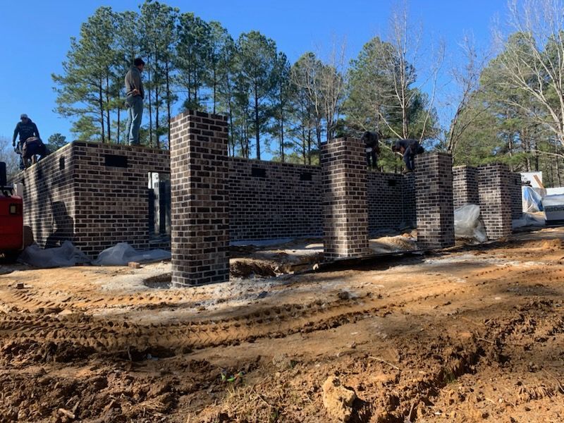 A brick building is being built in the middle of a dirt field.