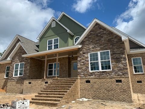 A large brick house with a green siding and stairs in front of it.