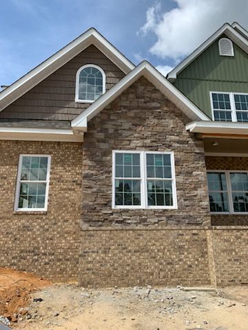 A brick house with white windows and a green roof is being built.